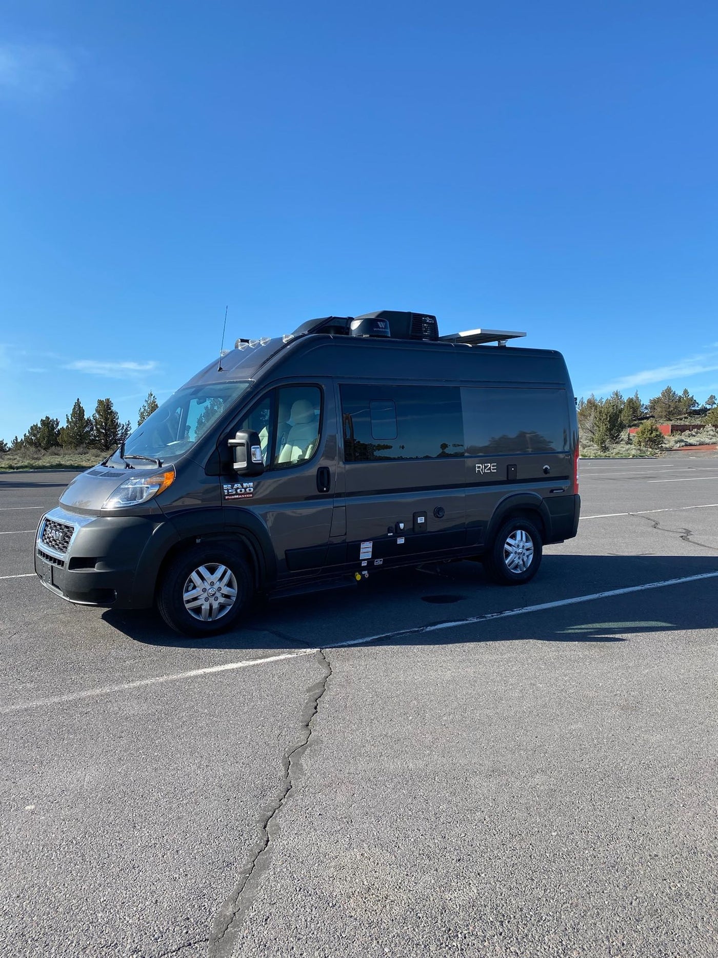 overlooking a stormy ocean with distant rocky islets under a grey sky.|Explore with this dark grey Ram ProMaster RV rental. This Rize camper van offers adventure travel — photo 5
