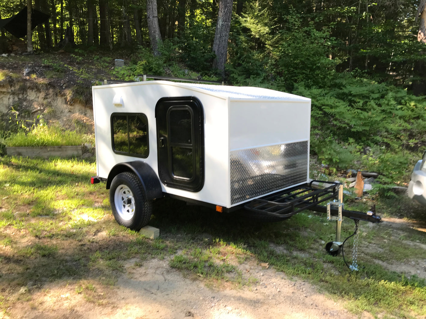 Experience nature with this white compact travel trailer. Perfect for an RV rental, it features a side door, window, and front rack.
