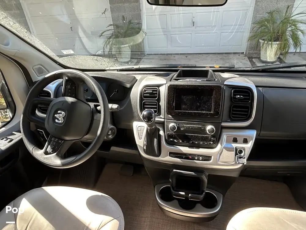 Modern RV rental interior: view of the dashboard, Ram steering wheel, infotainment display, and cup holders.