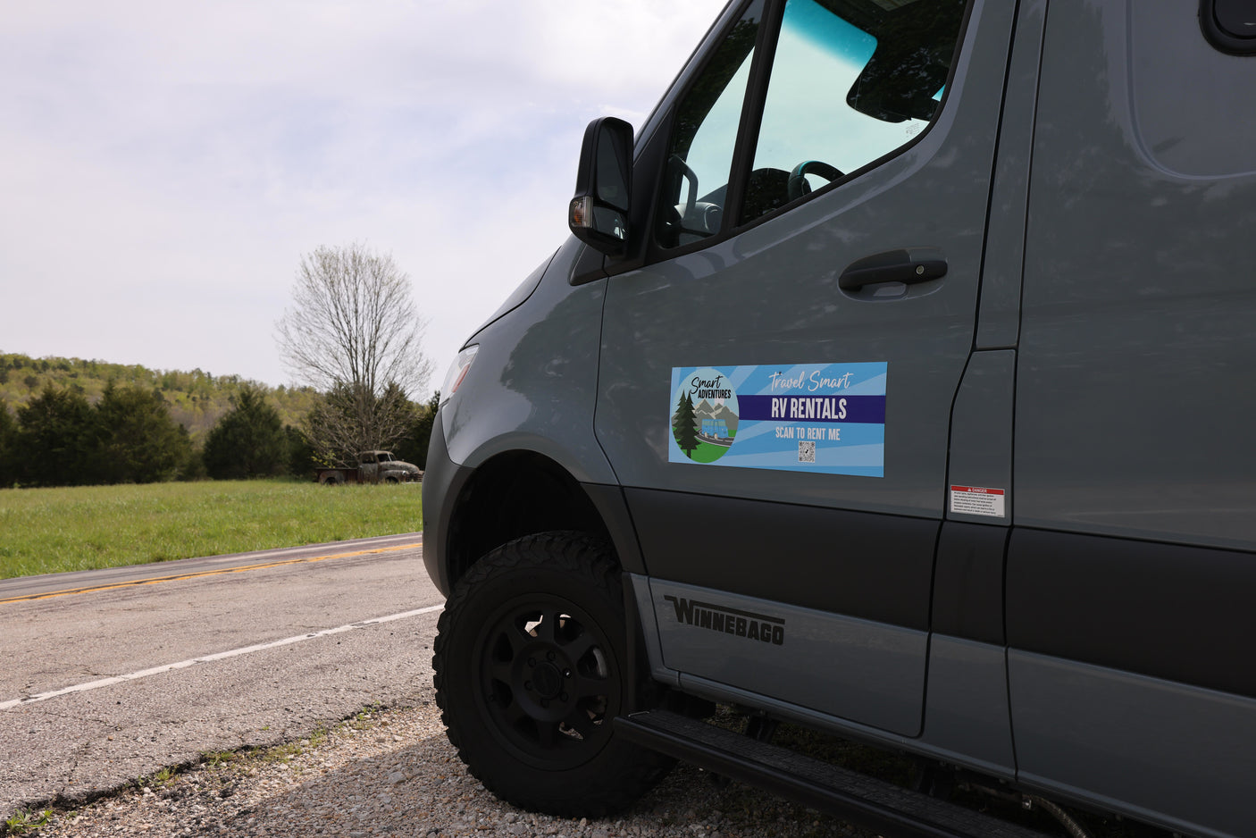Grey Winnebago RV rental parked roadside. Features "Travel Smart RV Rentals" magnet. Perfect for outdoor adventures.