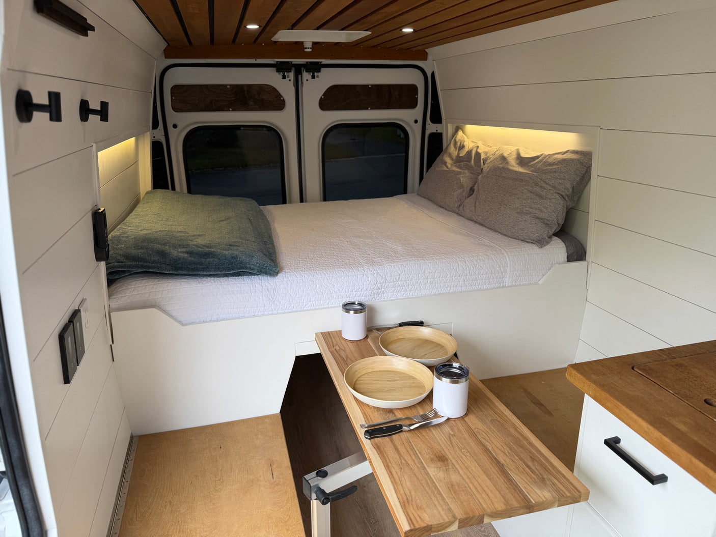 Cozy RV rental interior featuring a comfortable bed, warm wood ceiling, and a compact dining area with a pull-out table.