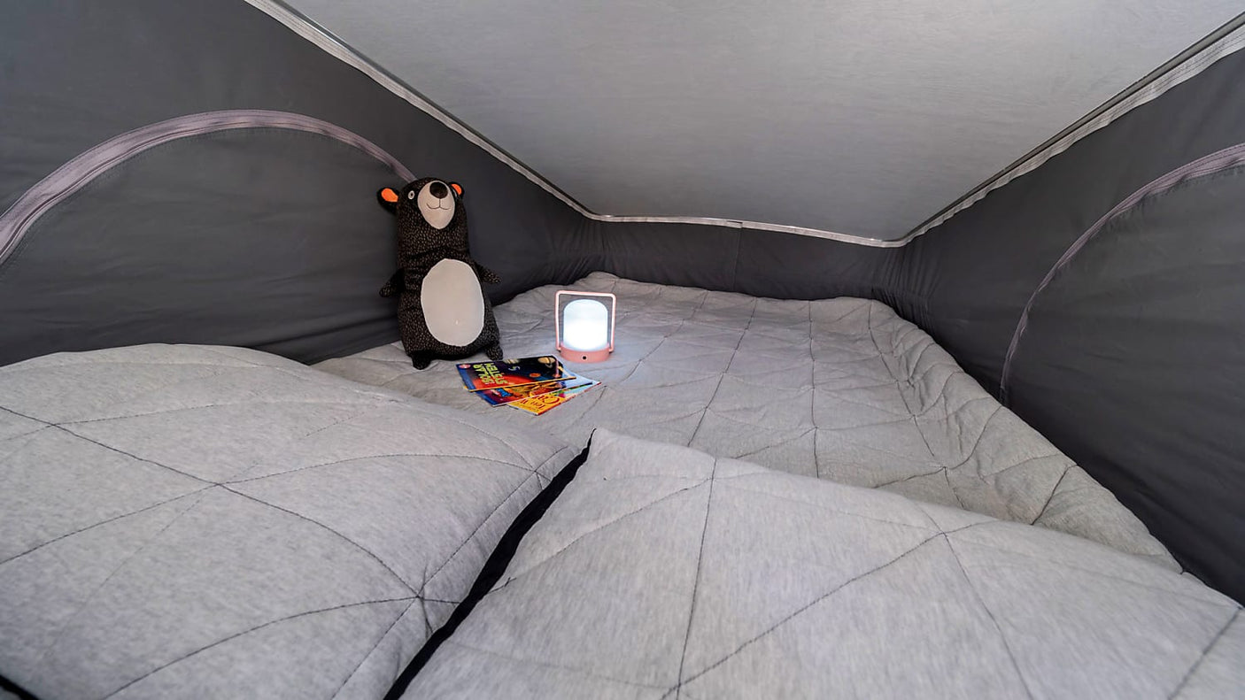 Cozy quilted bed inside an RV rental, featuring a plush bear and glowing lantern for comfortable camping nights.