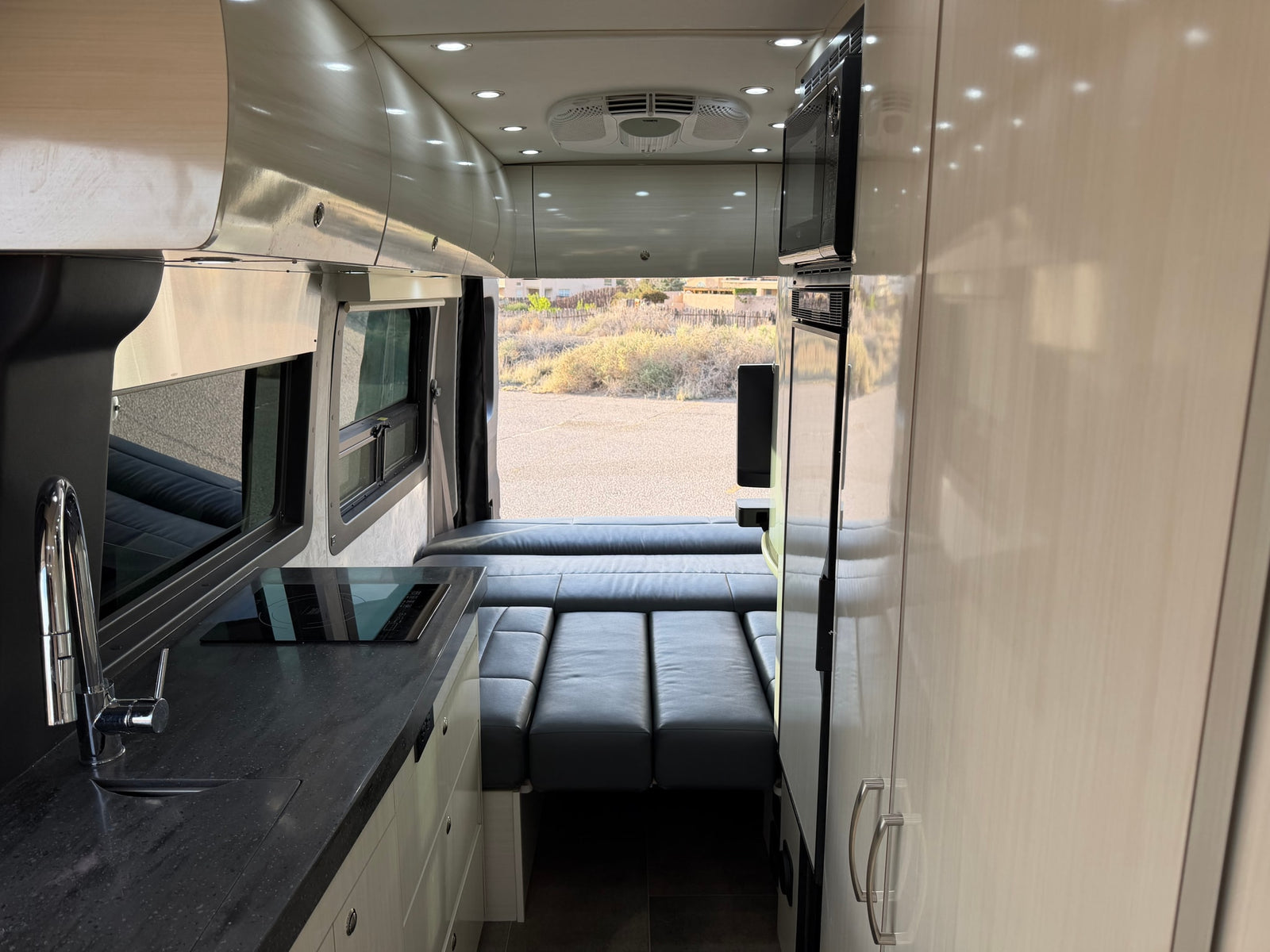 Modern rv rental interior with a compact kitchen, overhead cabinets, and convertible seating/bed, ideal for travel.