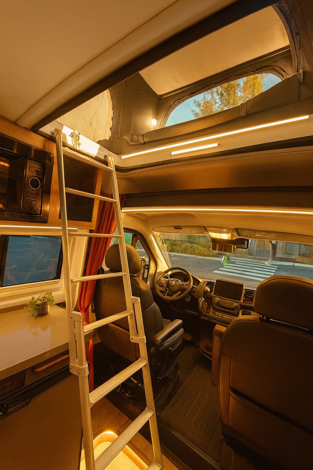 Inside an RV rental: ladder to a pop-top bed, microwave, counter, and driver's area, bathed in warm, inviting light.