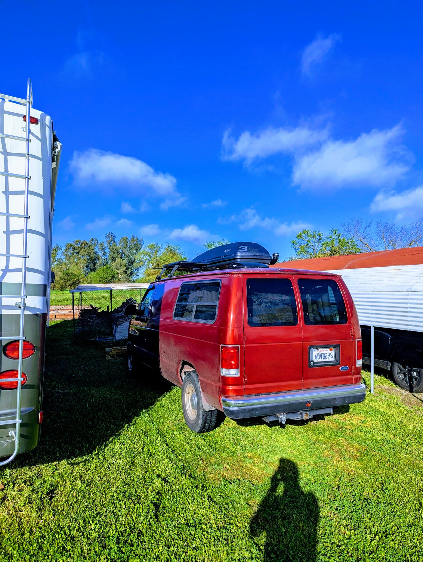 A red van with a roof box and an RV are parked on vibrant green grass under a clear blue sky. Great for an rv rental trip!