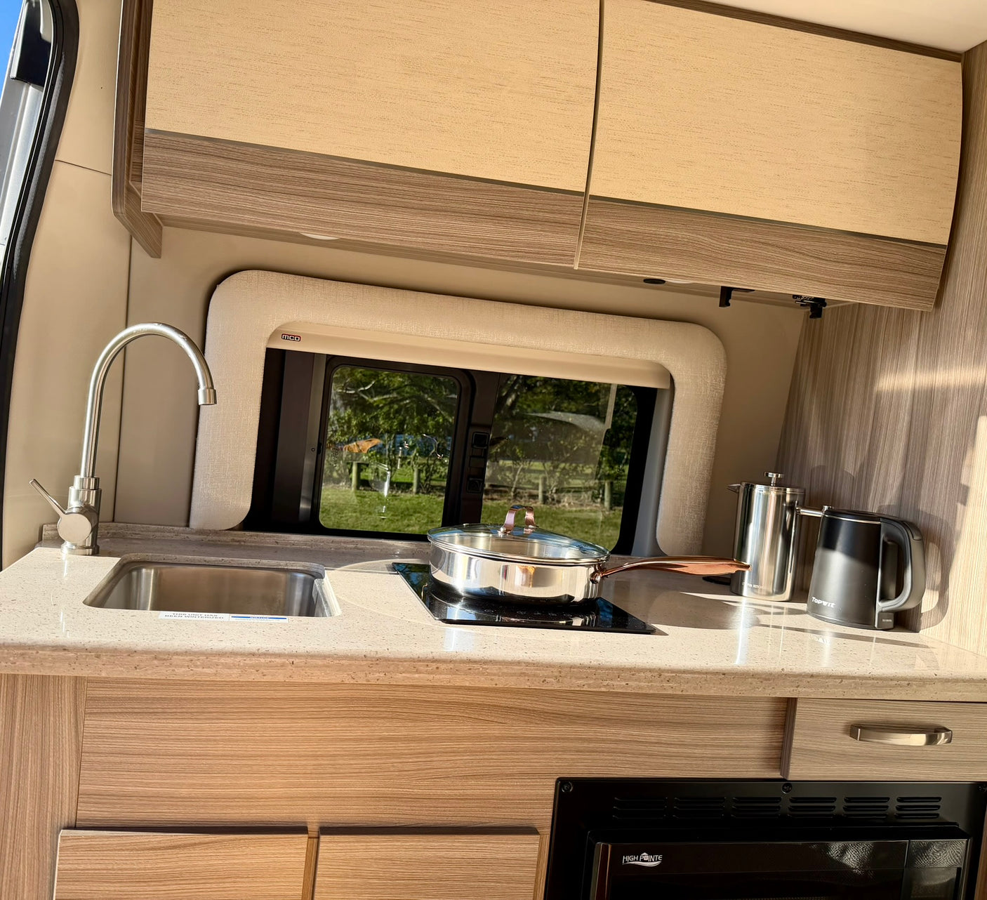 Modern RV rental kitchen featuring a sink, induction cooktop, microwave, and a scenic outdoor view.
