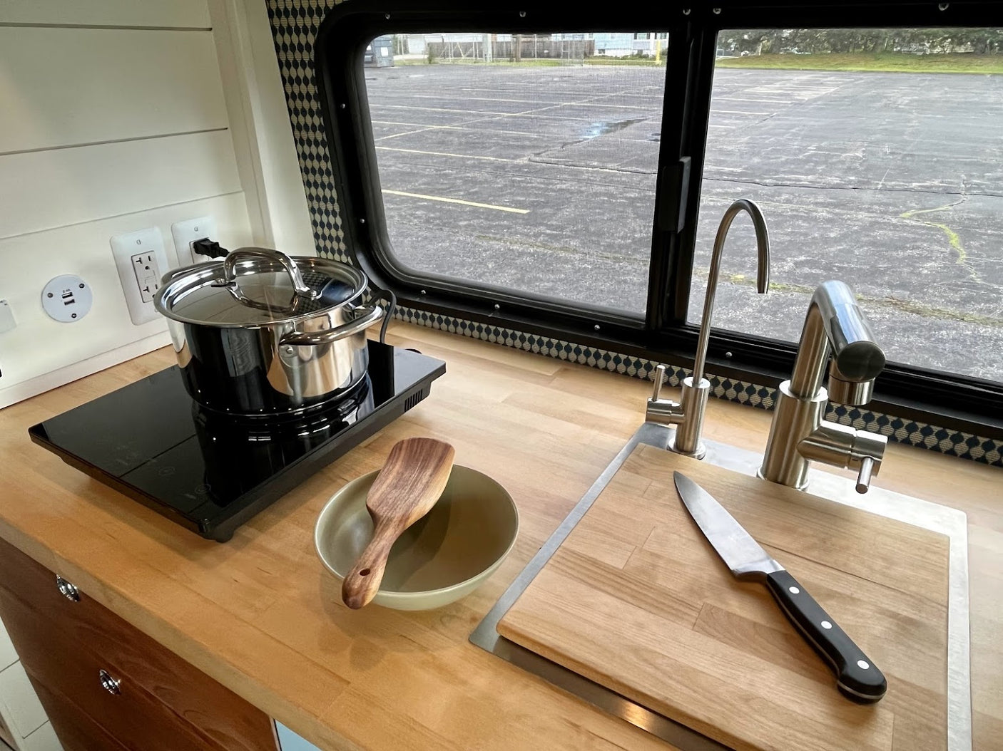 Modern RV rental kitchen with induction cooktop, sink, and wood counter. Perfect for cooking on the road.