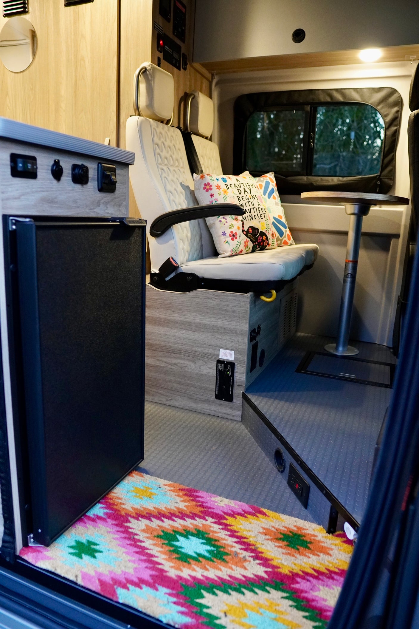 Cozy RV rental interior showcasing comfortable seating, an adjustable table, compact fridge, and a vibrant rug.