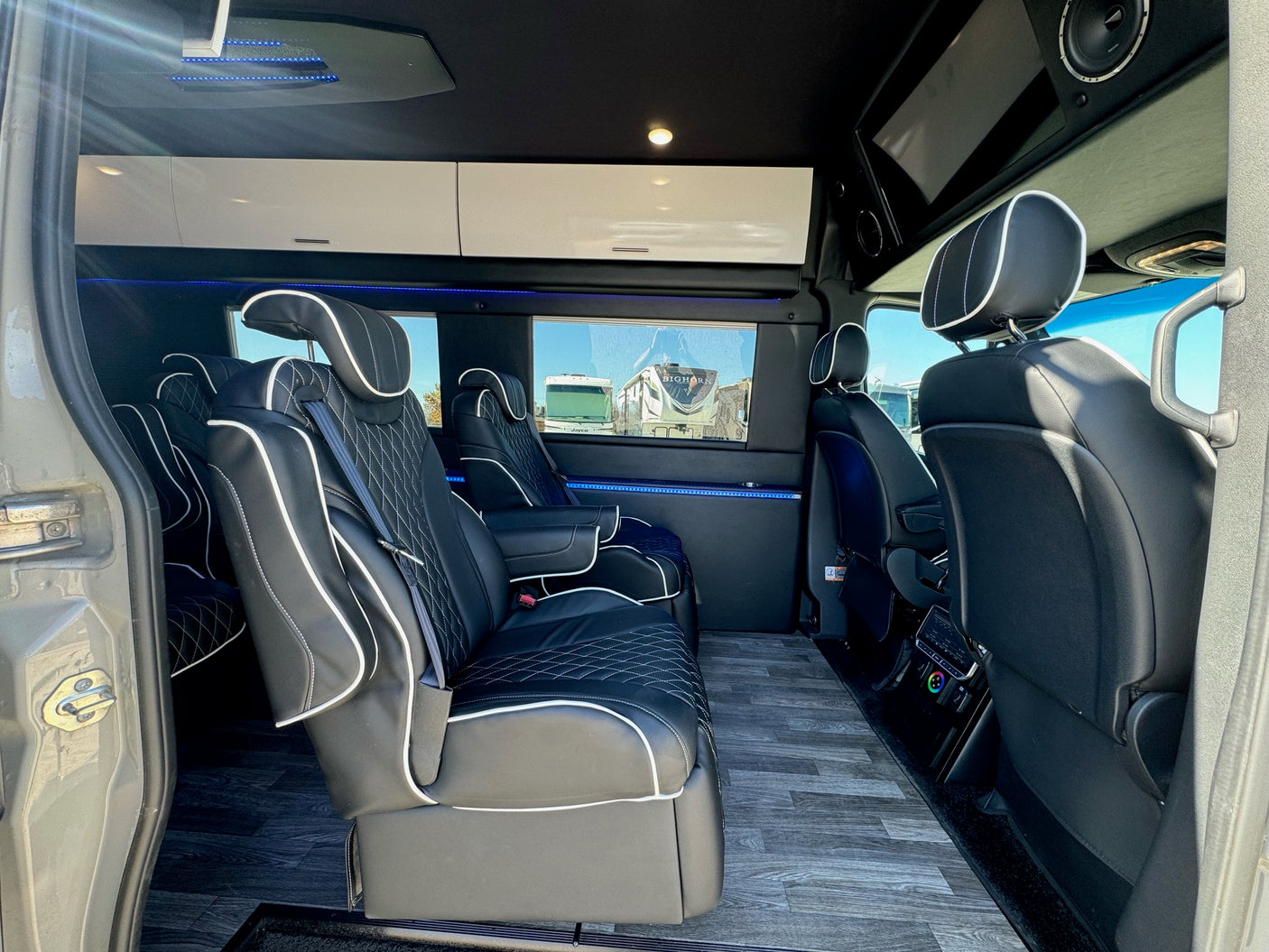 Luxury RV rental interior: spacious van with black leather captain's chairs, wood-look floor, and ambient blue LED lighting.