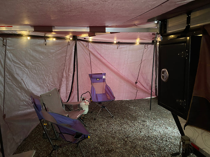 Spacious interior of an RV rental annex with camping chairs, string lights, and a gravel floor for outdoor comfort.