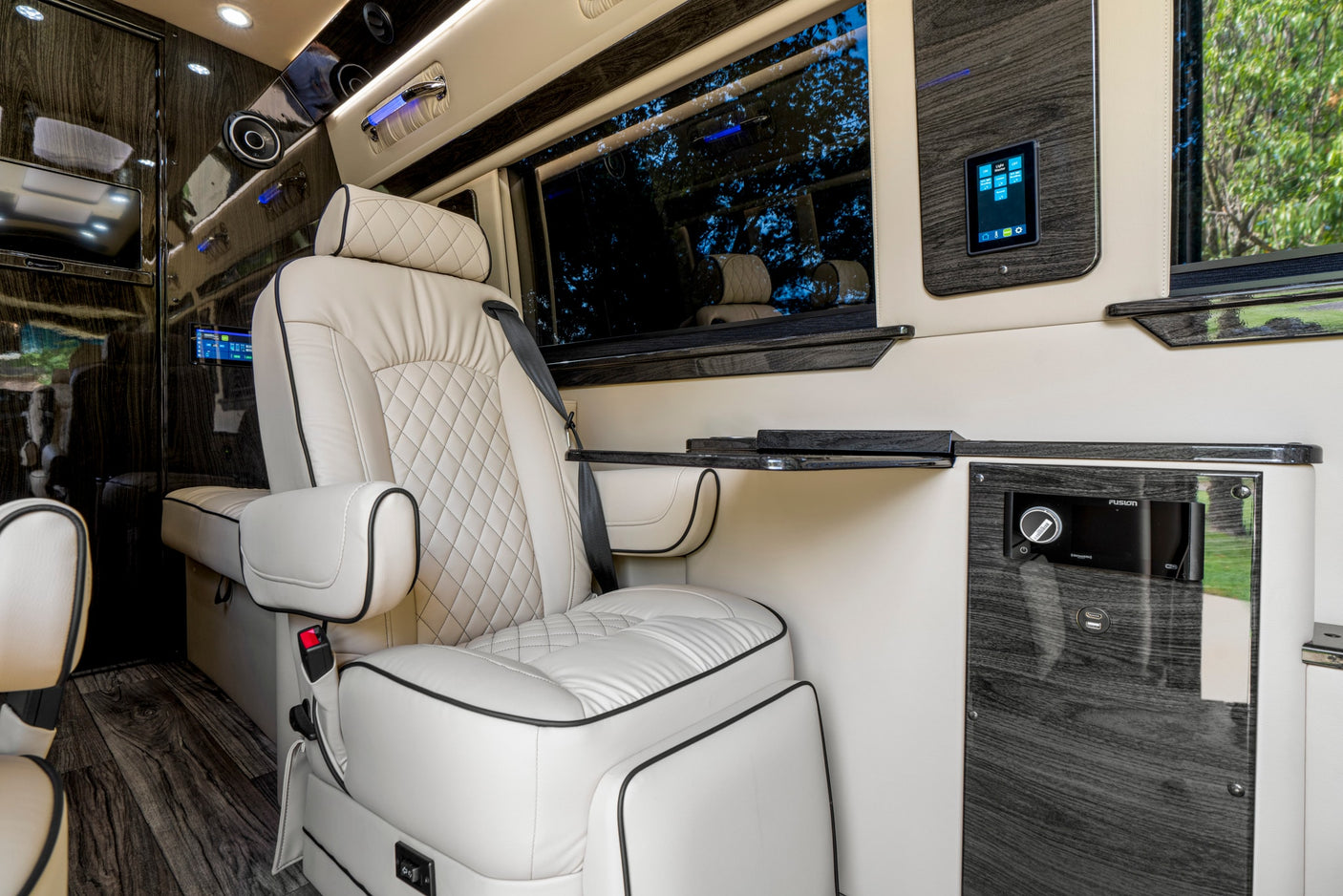Luxurious white leather passenger seat in a premium RV rental, featuring wood accents, a folding table, and digital controls.