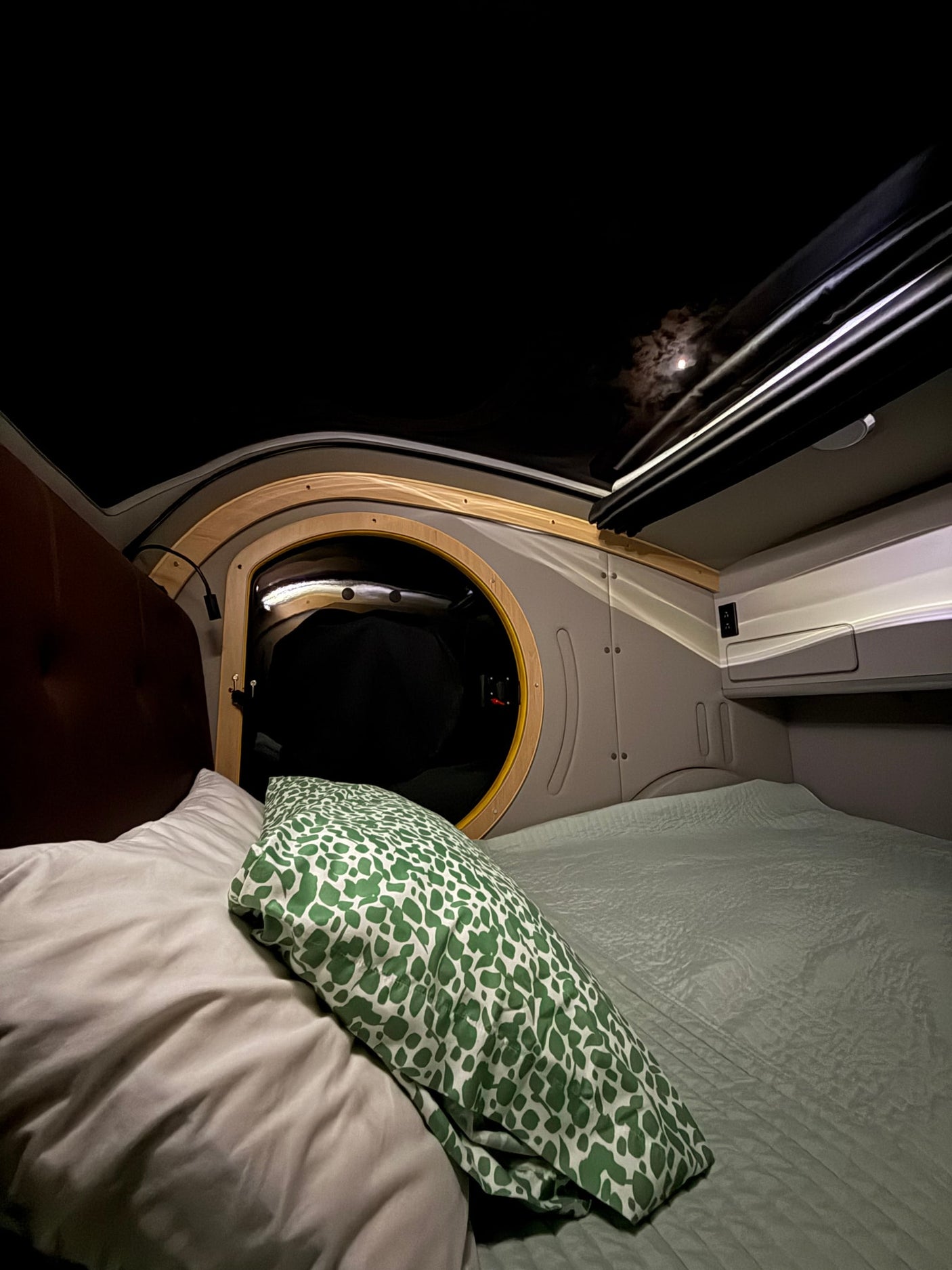 Cozy RV rental interior at night. The full moon shines through the roof opening, illuminating a comfortable bed with a green pillow.