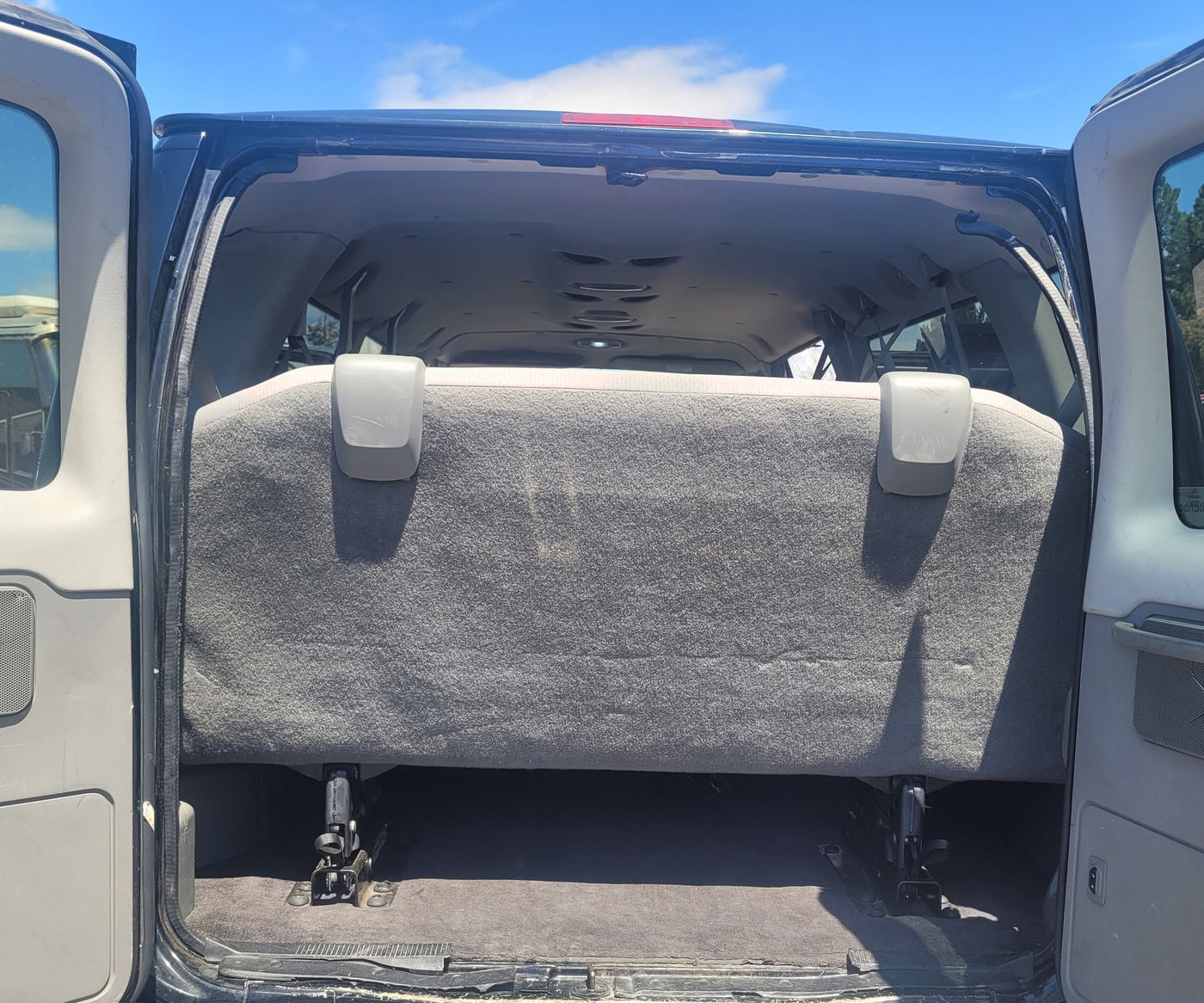 indicating an RV rental facility.|Inside an RV rental: multiple rows of gray fabric seats with visible seatbelts and buckle mechanisms. Other RVs are outside.|Spacious RV rental interior: rear view with open doors — photo 6