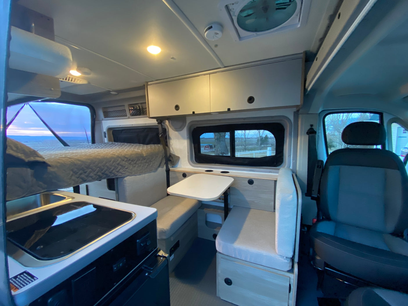 Interior of an RV rental camper van, featuring a bed, kitchenette, and dining area under warm lighting.