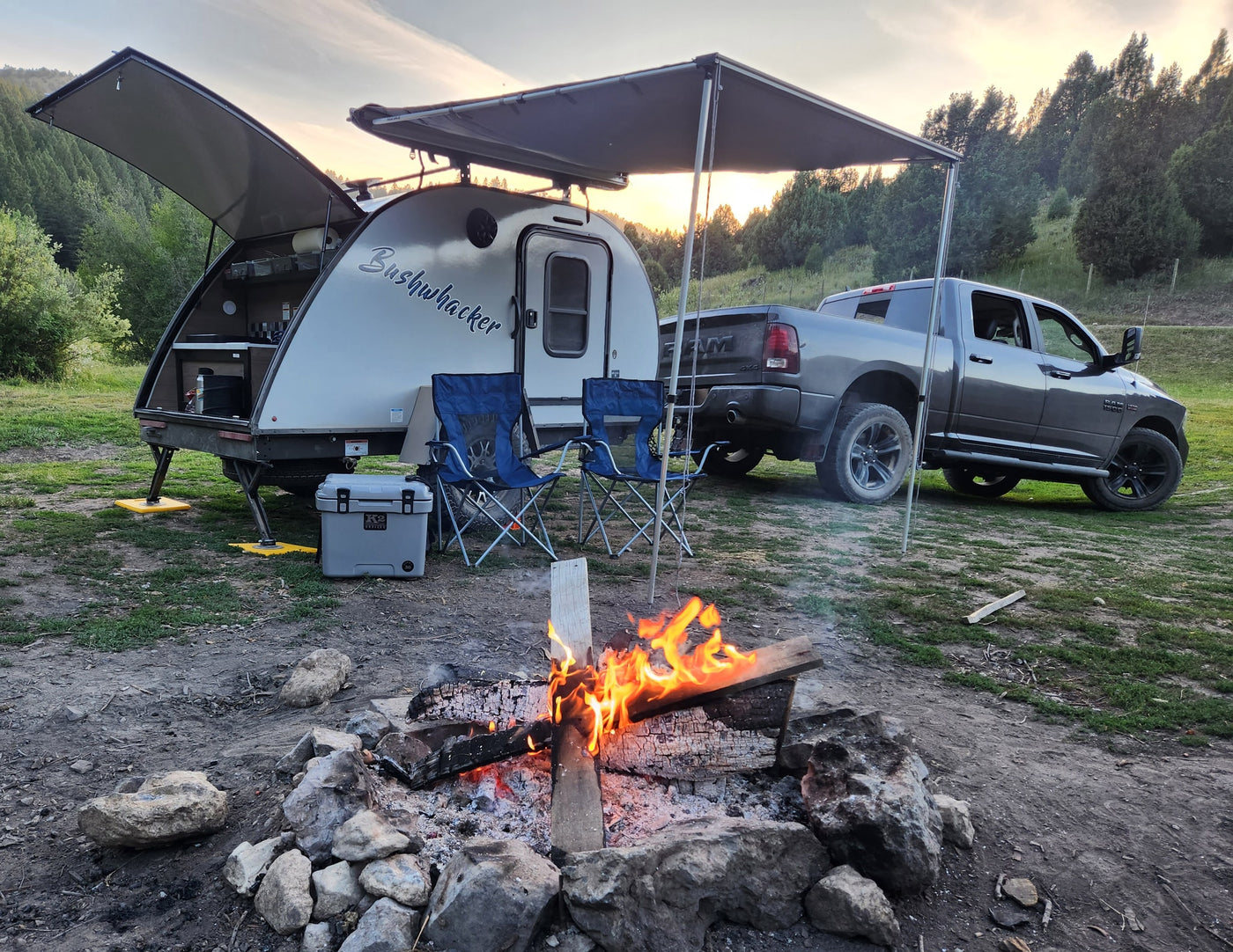 Cozy RV rental setup: Teardrop trailer, truck, and warm campfire under a sunset sky, perfect for outdoor camping adventure. — photo 1
