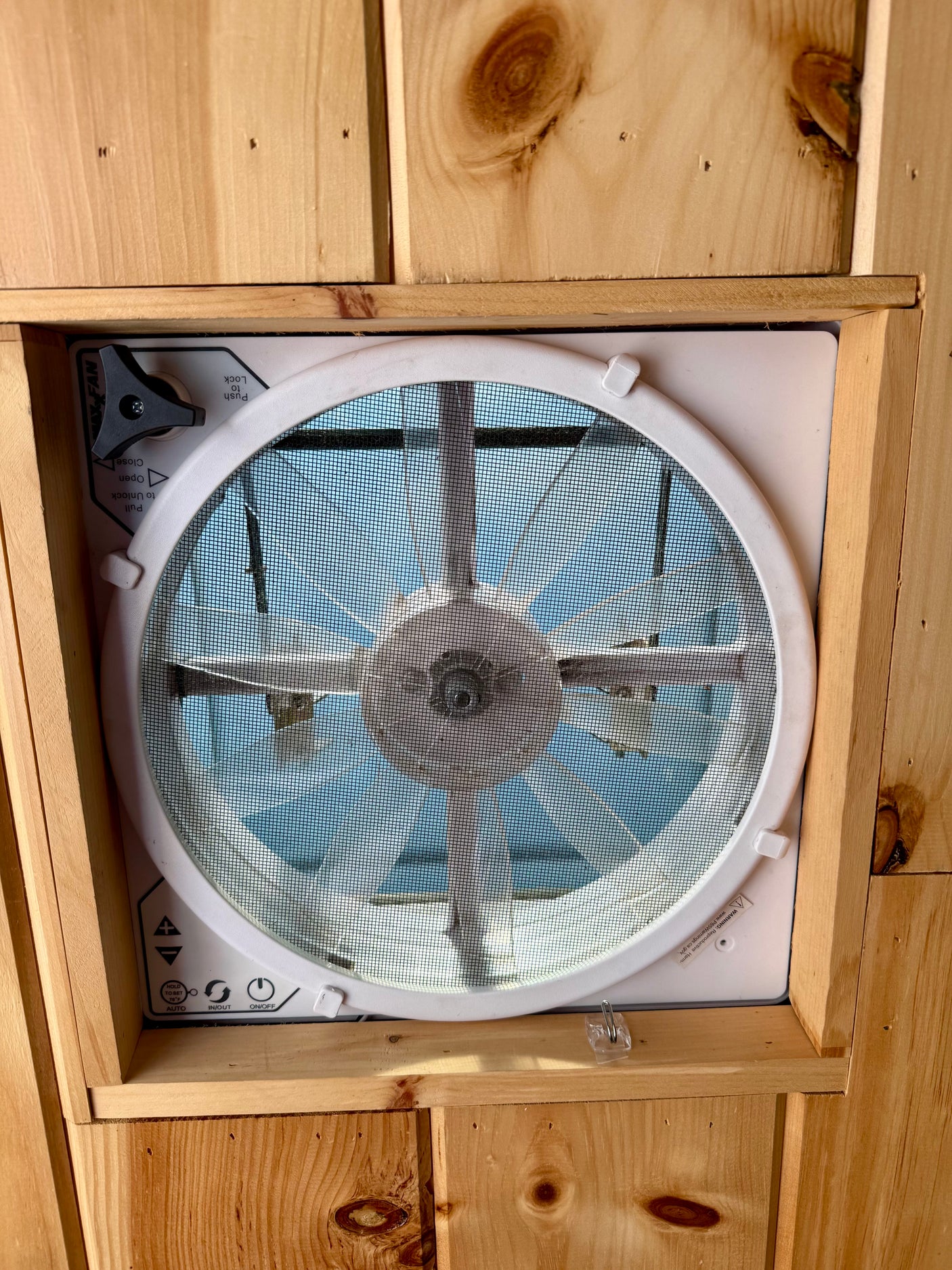 RV rental interior: White ceiling fan with mesh screen & controls in natural wooden paneling, providing fresh air.