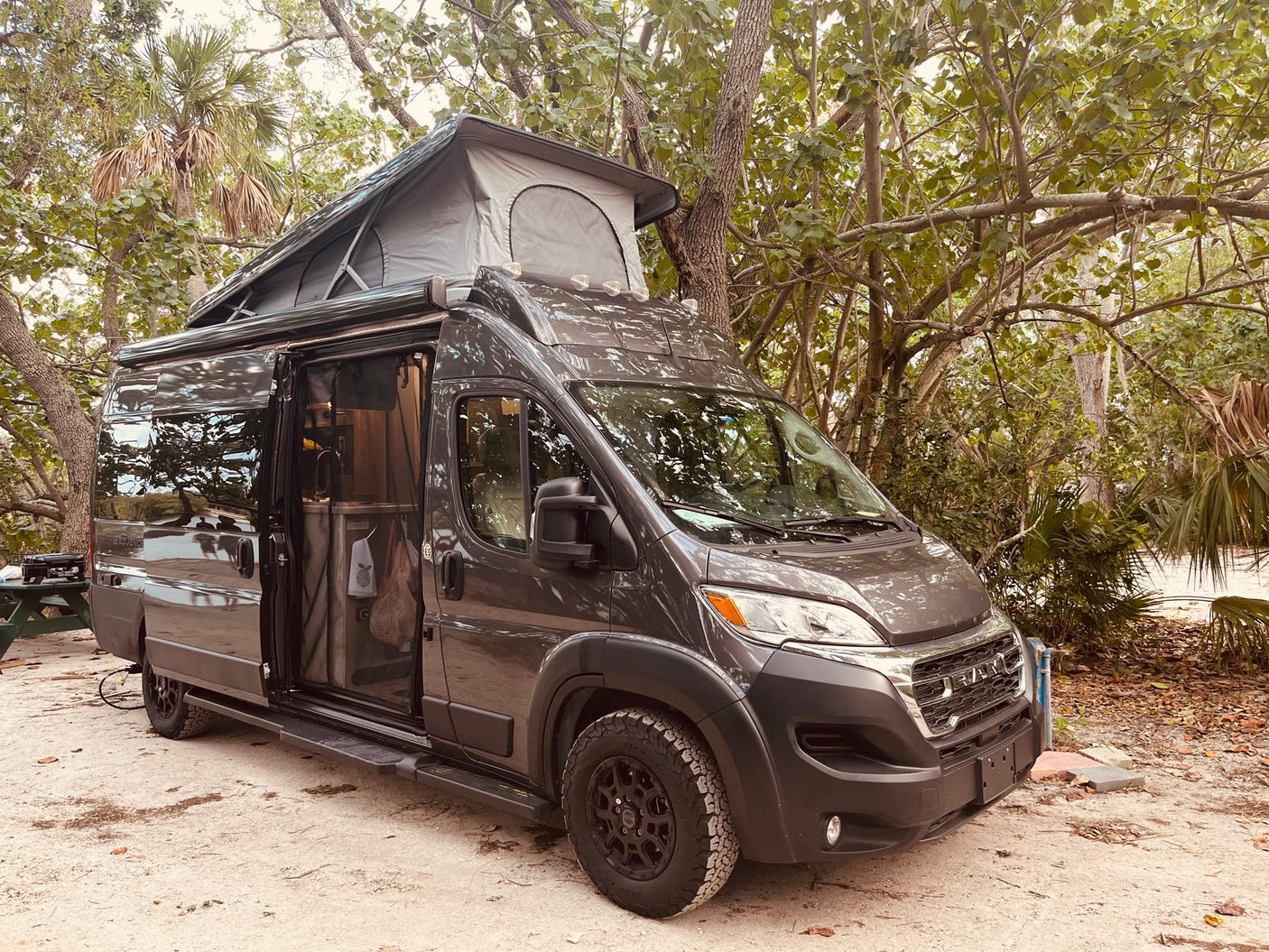 This dark gray pop-top RV rental camper van is parked at a scenic campsite, ready for your outdoor travel adventure.