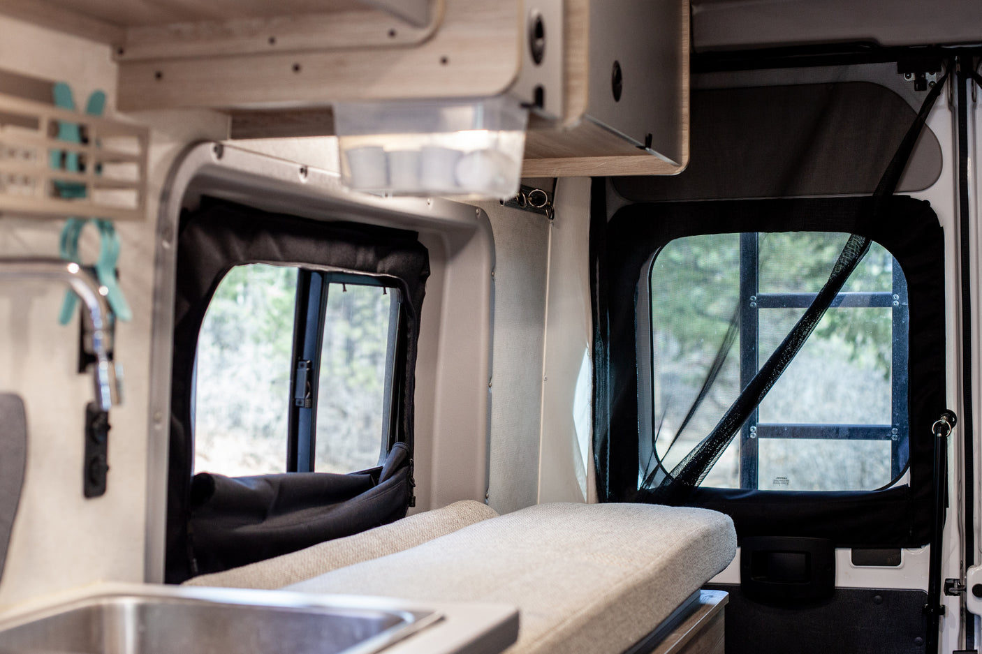 Inside this inviting rv rental, a camper van interior with comfortable seating, a small kitchen, and large windows with nature views.