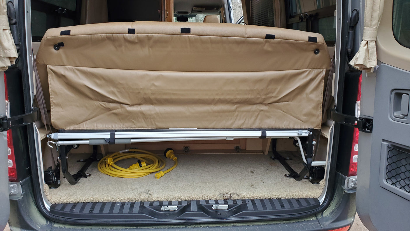 Camper van RV rental: rear interior shows a raised bed, revealing carpeted storage with a yellow power cable.
