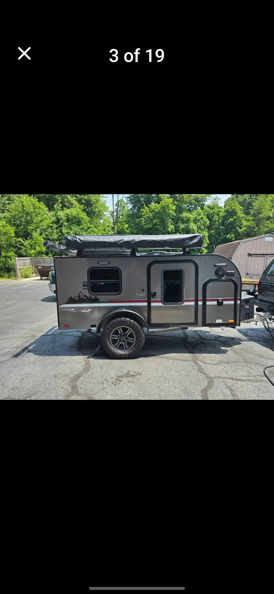 Rugged gray teardrop camper trailer, ideal for an rv rental adventure. Features off-road tires & roof rack, parked on asphalt.
