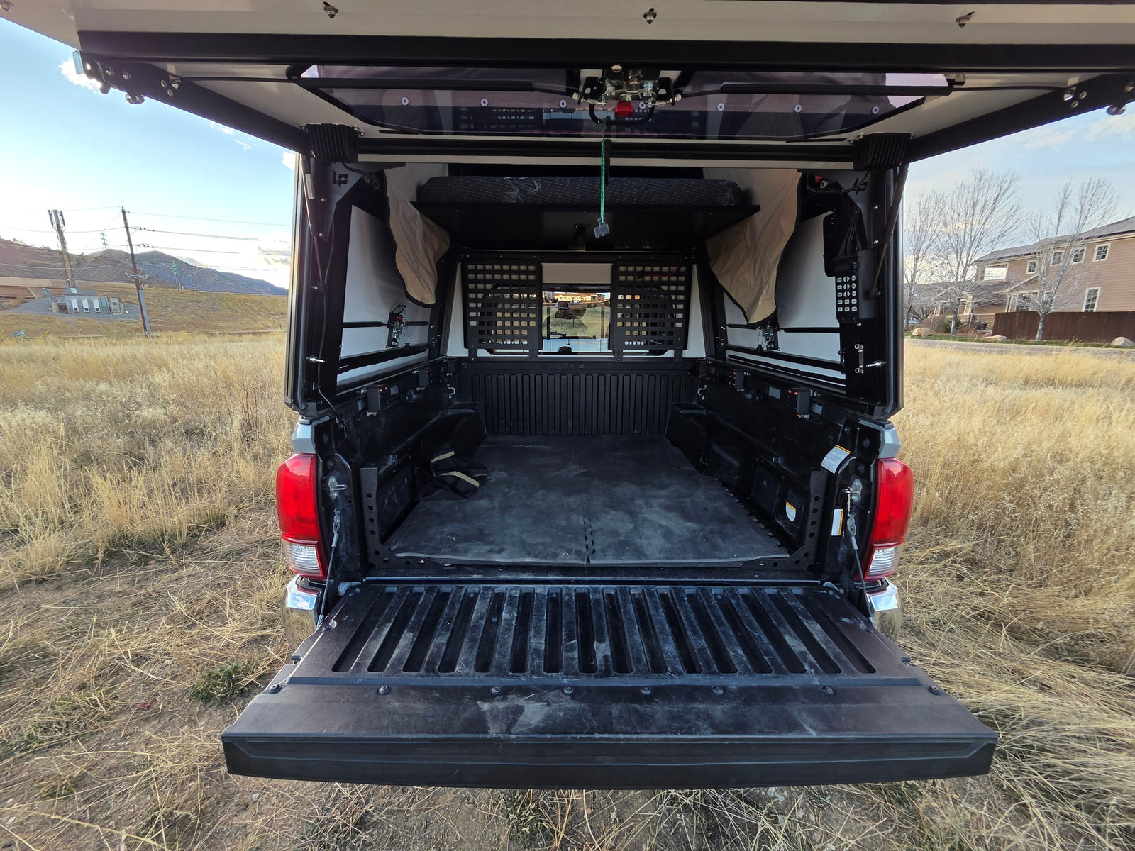 The open tailgate of an overland truck camper reveals a custom bed and storage for adventures. A unique RV rental option.