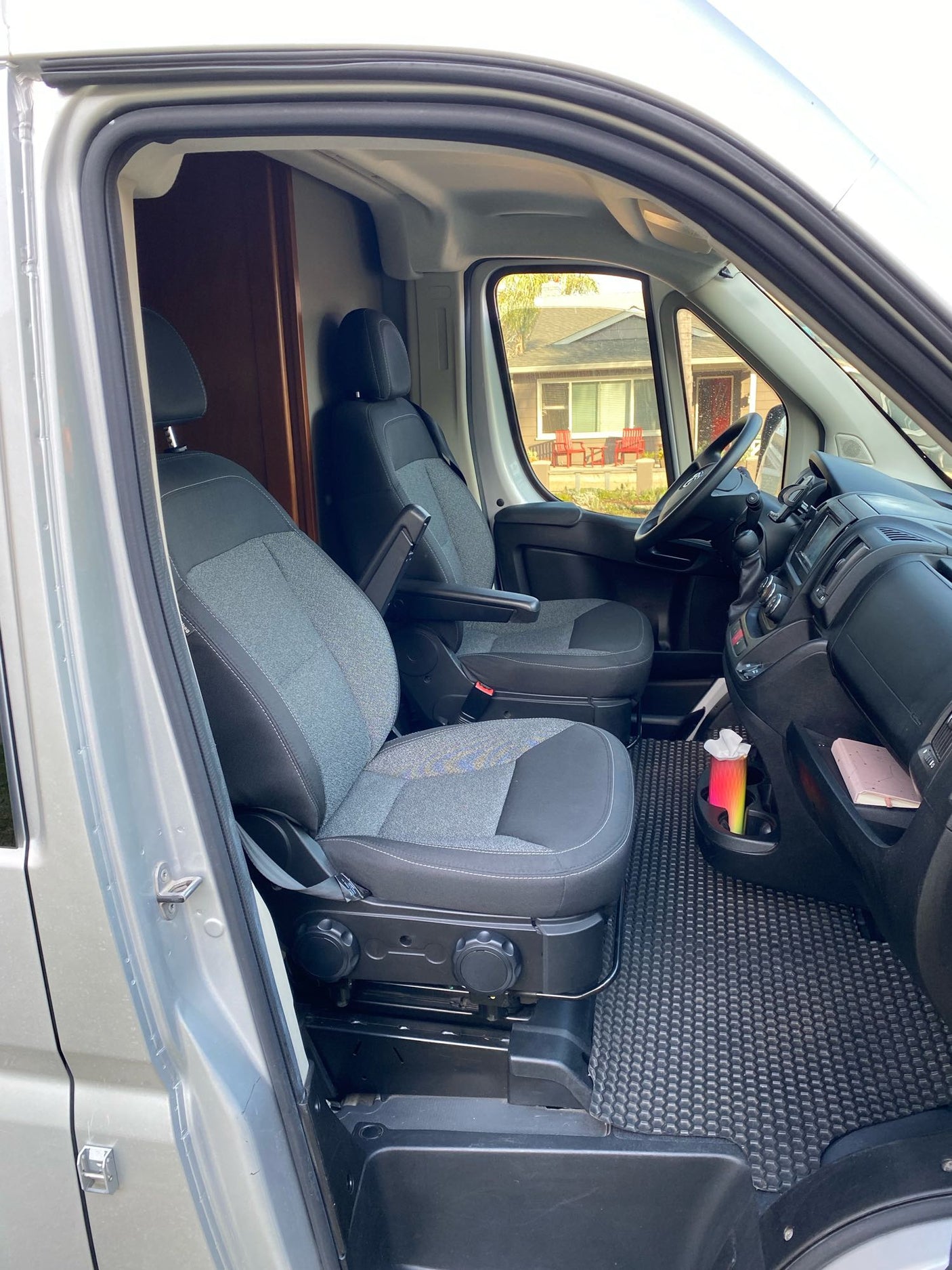 RV rental: Front cabin of a converted van, featuring two gray seats, dashboard, and custom rear partition.