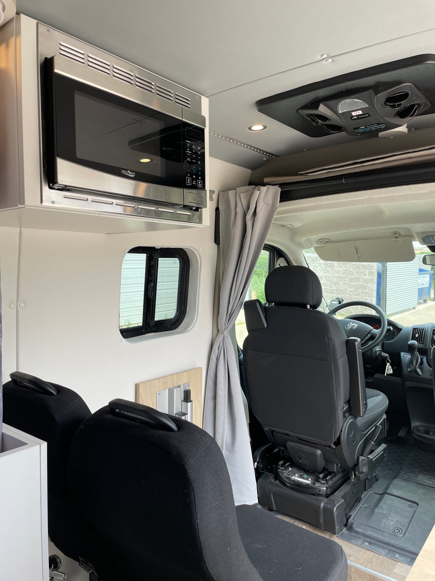 Modern RV rental interior showing microwave, passenger seats, and ceiling cooling unit, ready for adventures.