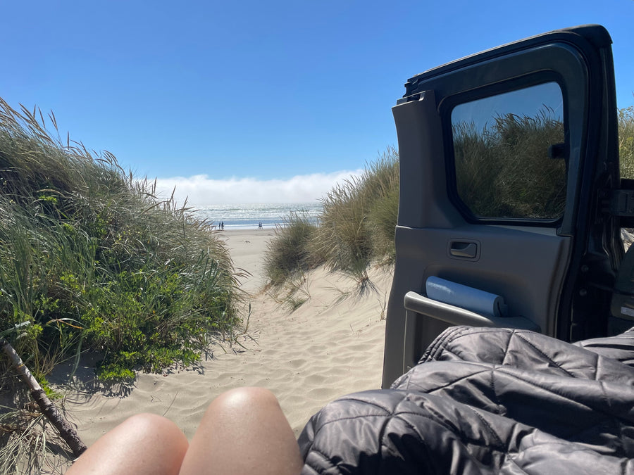 Legs out, enjoying the sunny beach view of sand dunes and ocean from an RV rental.
