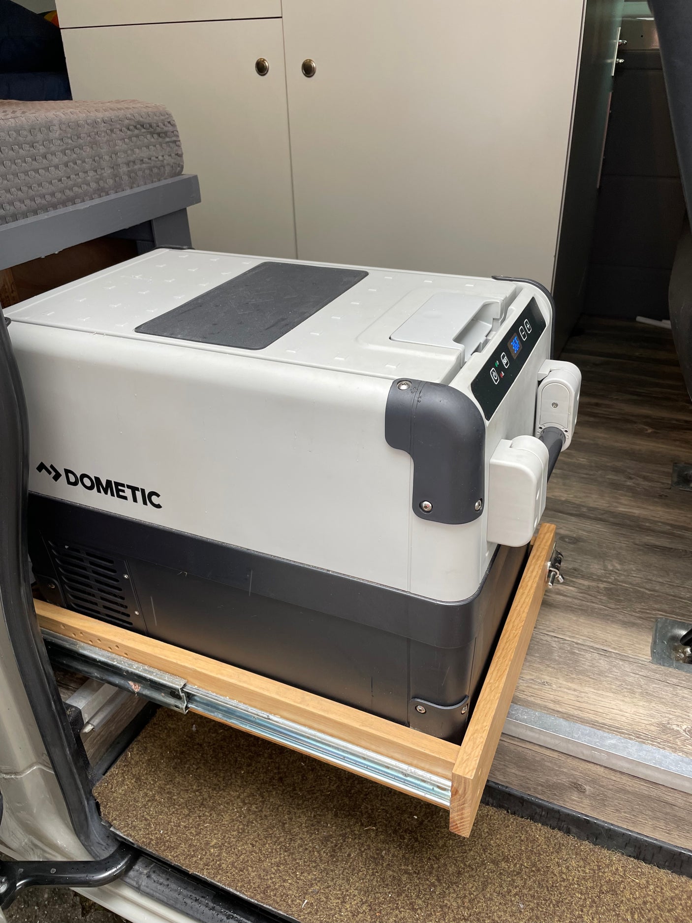 A Dometic portable fridge on a pull-out slide system, installed in an RV rental with wooden floors and cabinets.