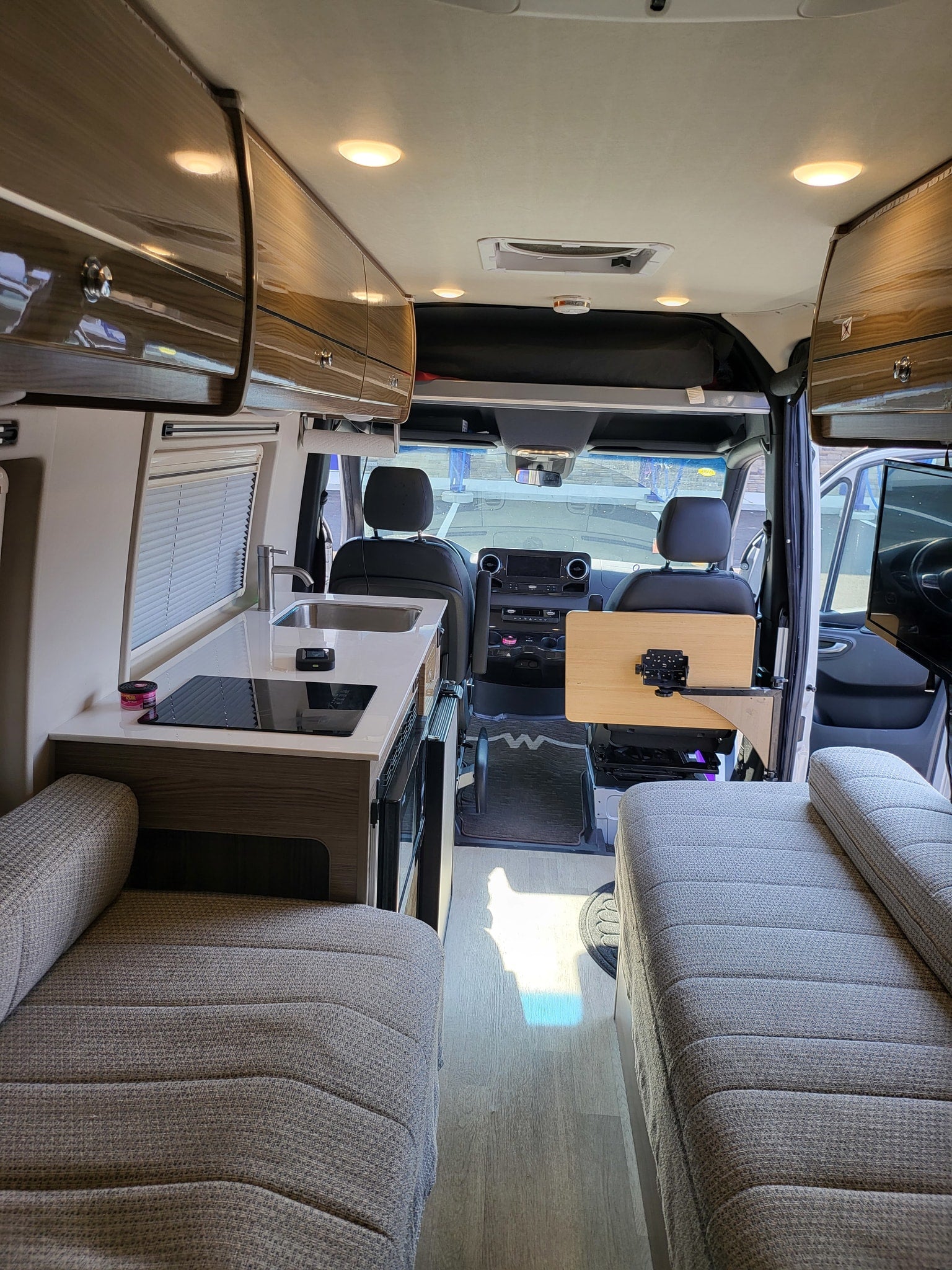 Inside a sleek RV rental, showcasing a compact kitchen, comfortable seating, and front cockpit area for travel.