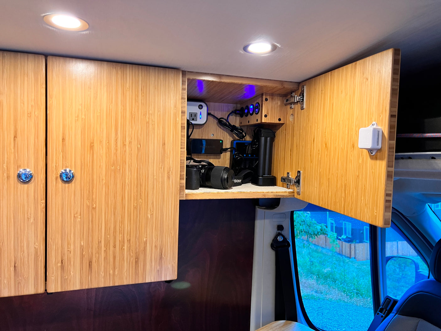 RV rental: Organized camper van interior featuring overhead bamboo cabinets, a charging station for camera gear, and LED lights.
