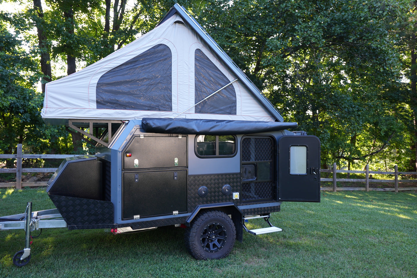 RV rental: A gray and black off-road adventure trailer with an open pop-up tent and storage, ready for camping.