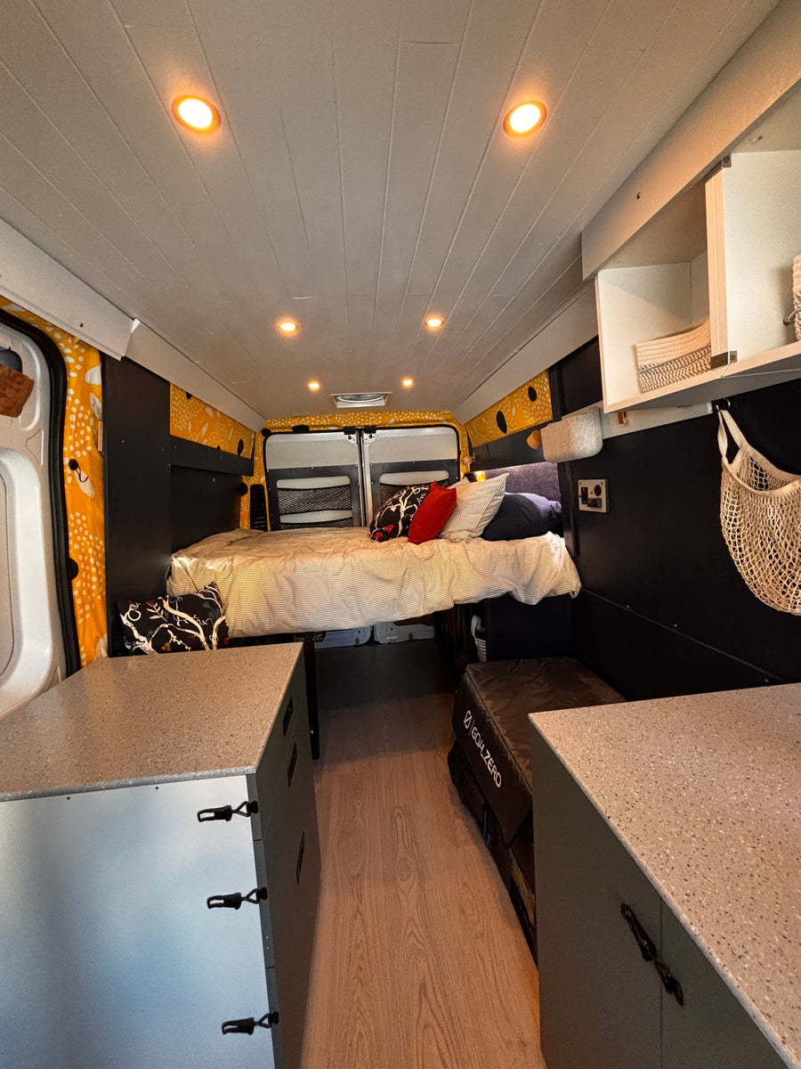 Spacious rv rental camper van interior: cozy bed, overhead lights, built-in storage, and wood-look flooring for comfort.