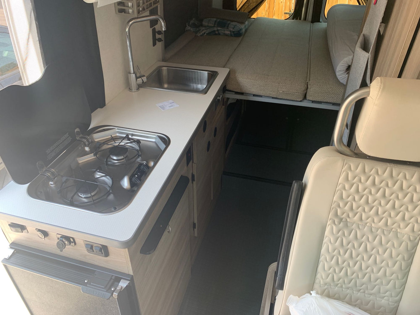 RV rental interior: A bright, compact camper van featuring a kitchenette with stove and sink, plus an elevated bed above storage.