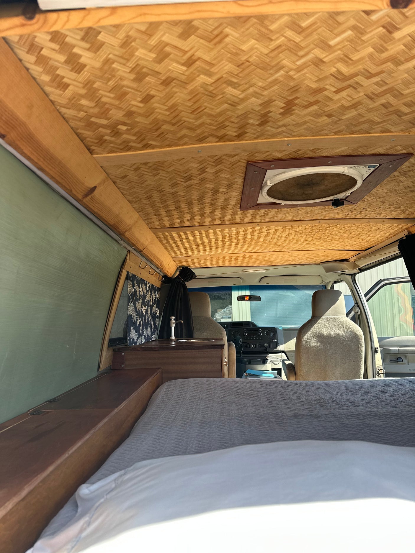 Cozy RV rental camper van interior with bed, patterned bamboo ceiling, small sink, and front cabin view.