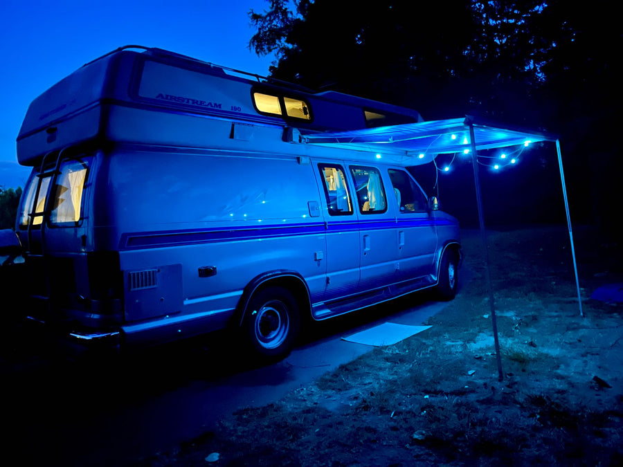 This RV rental, an Airstream van, is ready for adventure! Parked at night with blue awning lights and warm interior glow.