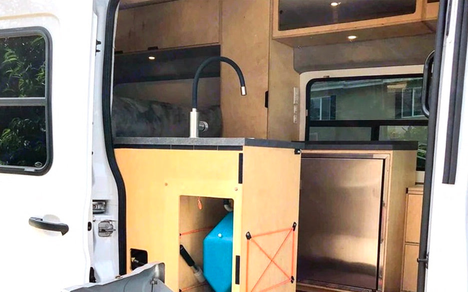 RV rental interior: a compact kitchen with a sink, flexible faucet, water tank, and built-in fridge, designed for van life.