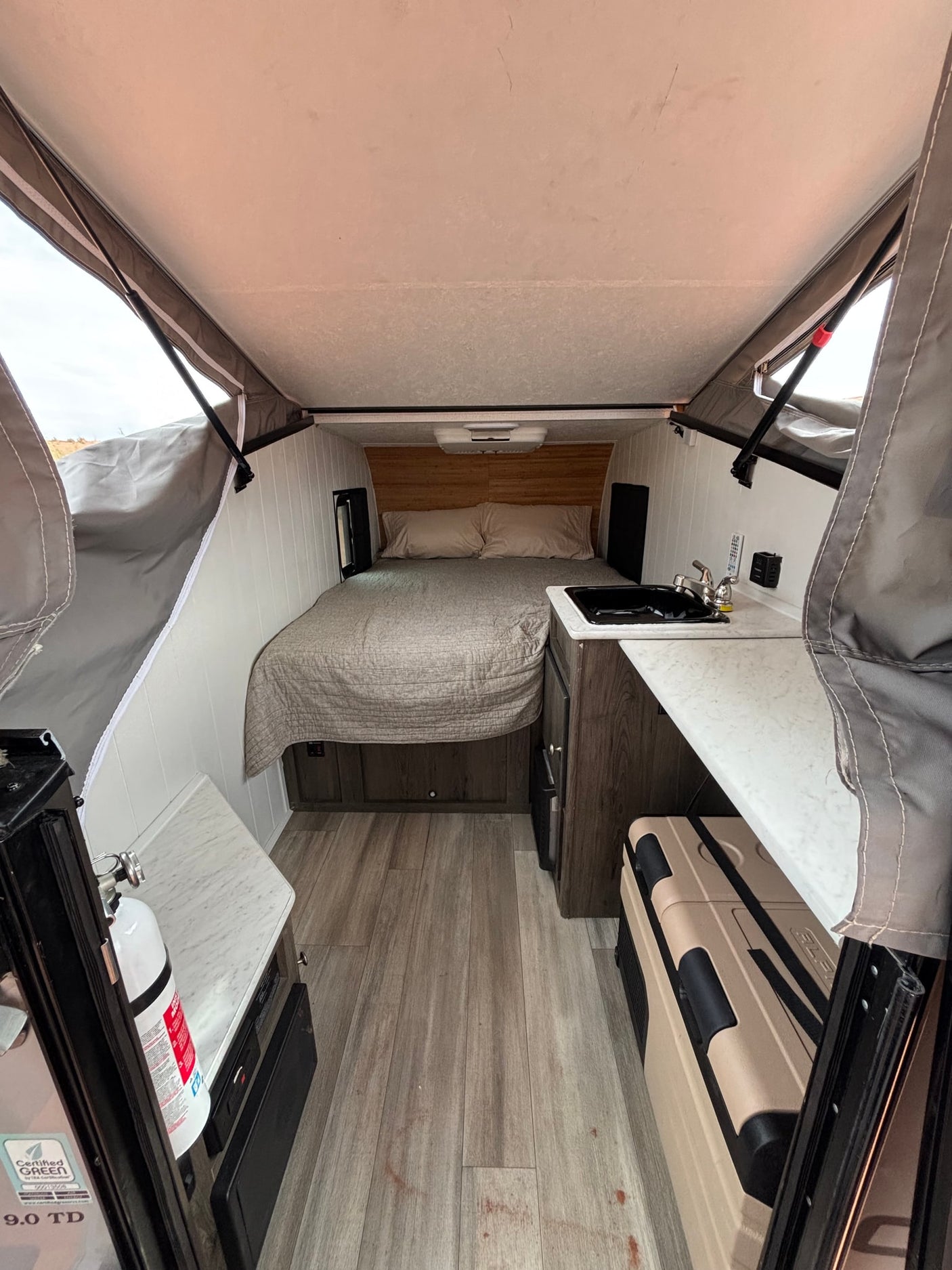 rests on red sand amidst towering red rock formations.|Adventure awaits with this Clipper RV rental camper in a stunning red rock desert under cloudy skies.|RV rental: a cozy pop-up camper interior with bed