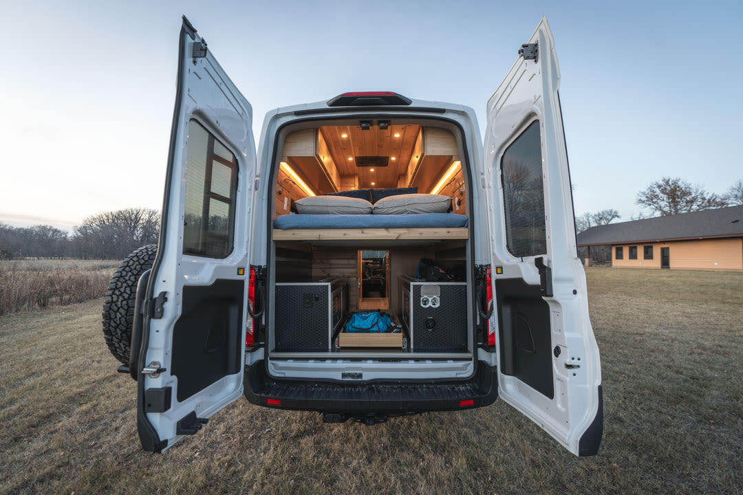 showcases its cozy wood interior through an open side door. Ready for adventure!|Experience a luxury RV rental interior: wood-paneled walls