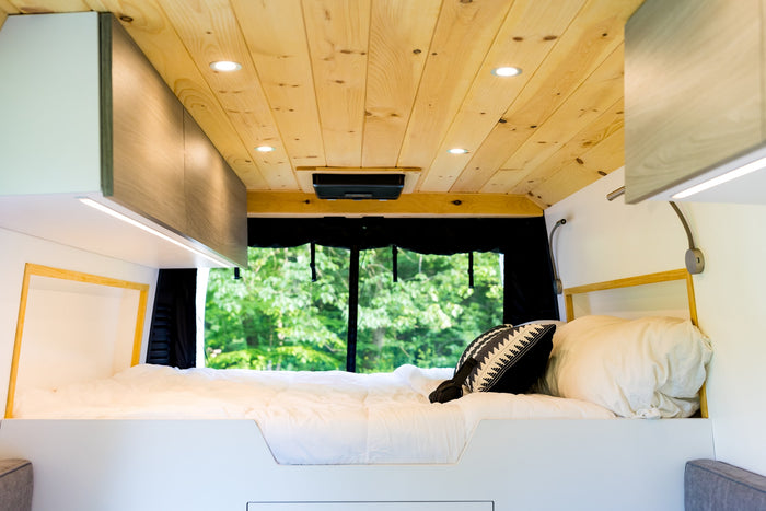 Cozy rv rental interior featuring a comfortable bed, warm wooden ceiling with lights, and a serene nature view.