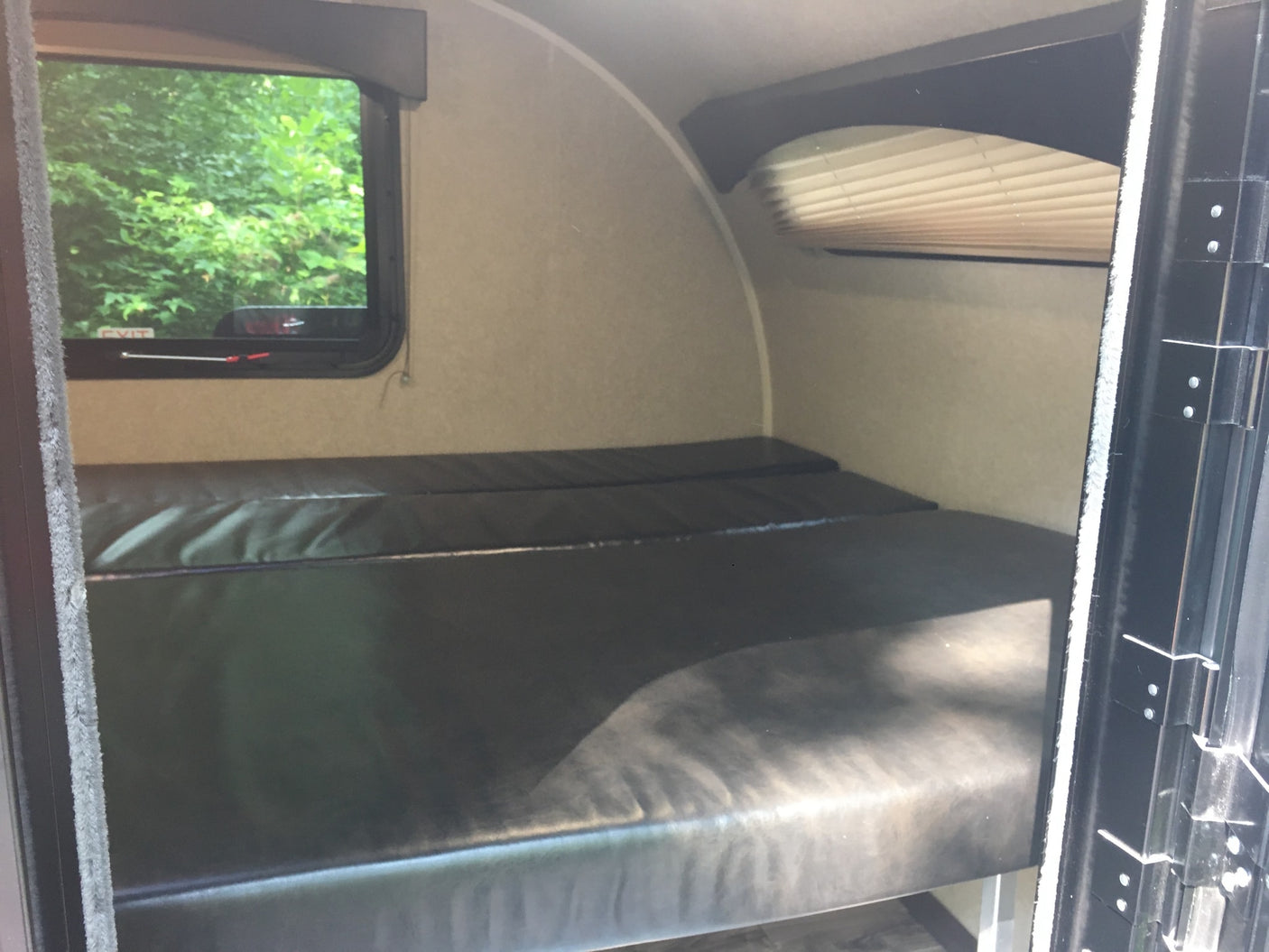RV rental with dark bunk beds, window overlooking trees. A compact camper interior sleeping space.
