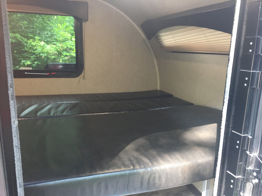 RV rental with dark bunk beds, window overlooking trees. A compact camper interior sleeping space.