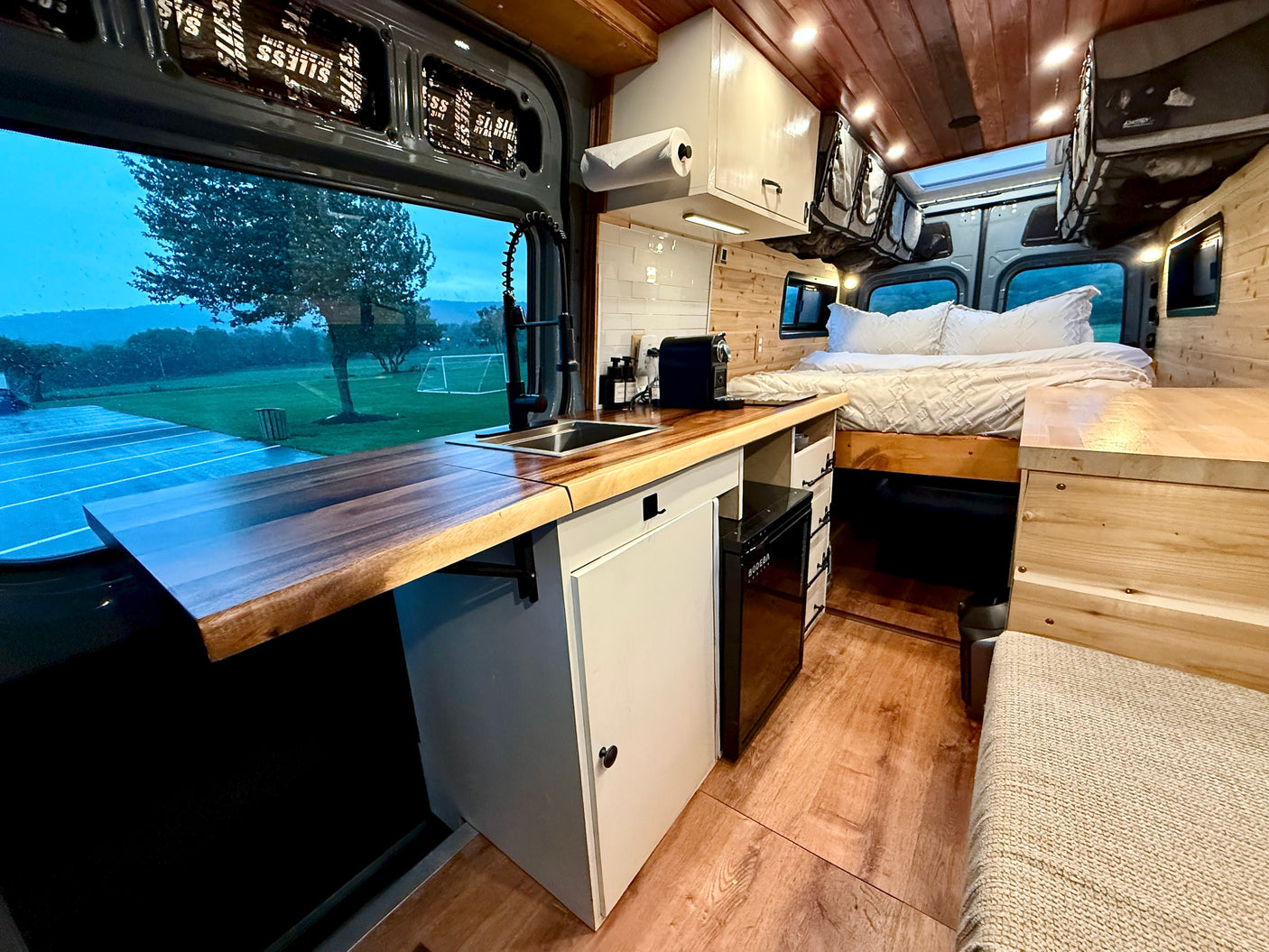 Step inside this cozy RV rental: a modern kitchenette with a sink, a comfortable bed, and a scenic outdoor view. Ideal for travel.