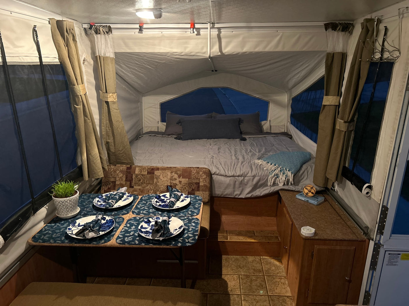 Explore this RV rental's cozy pop-up camper interior with a bed and dining area, ideal for glamping trips.
