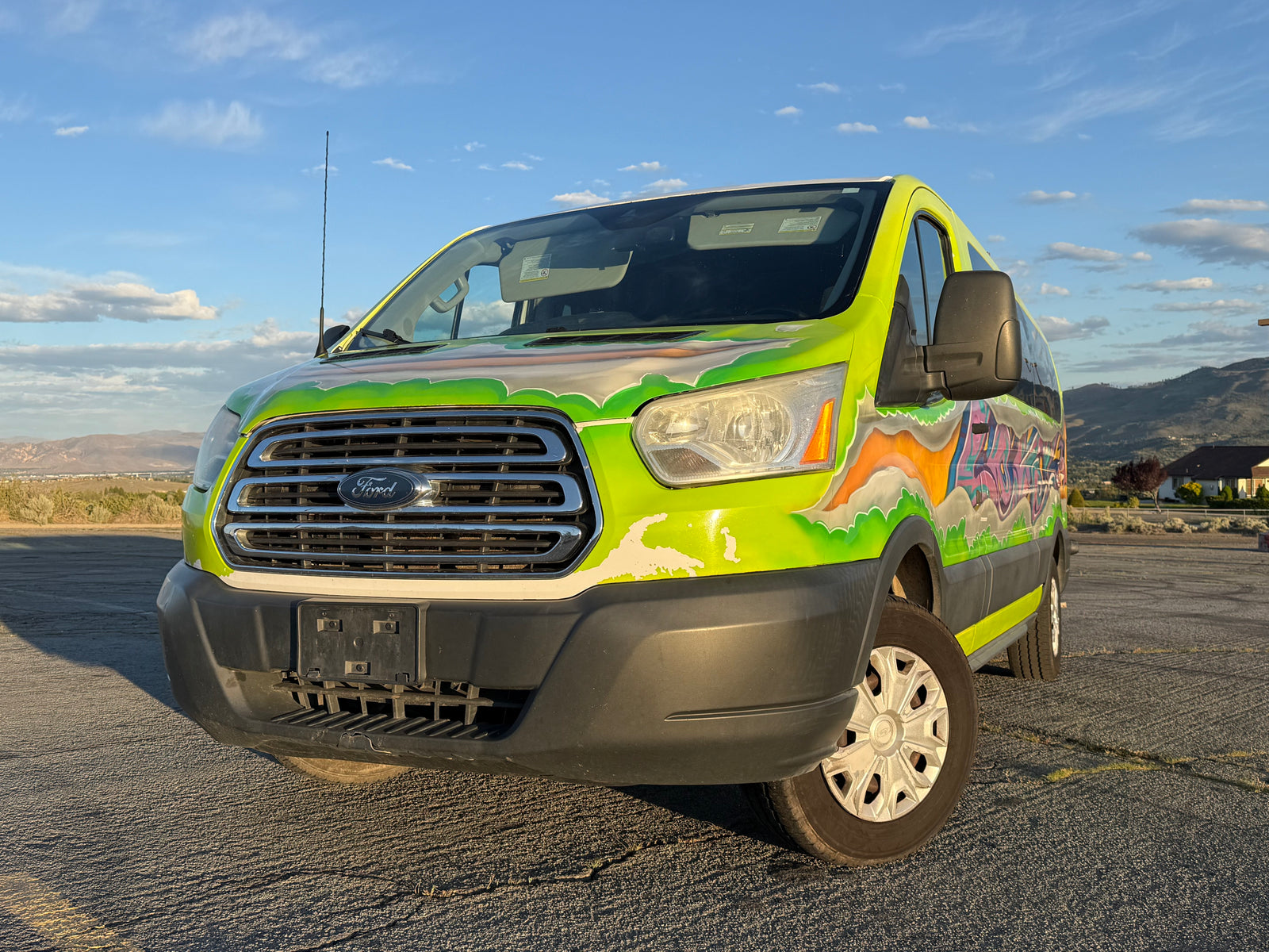 This custom-painted Ford Transit van, an eye-catching rv rental, features vibrant graffiti art, parked against a scenic mountain backdrop.