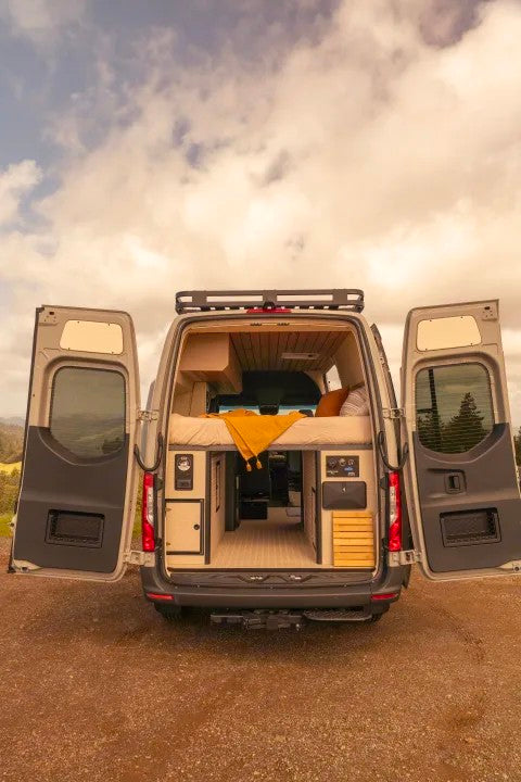Ready for adventure? This RV rental offers a peek into a custom camper van's open rear, revealing a comfy bed & functional interior.