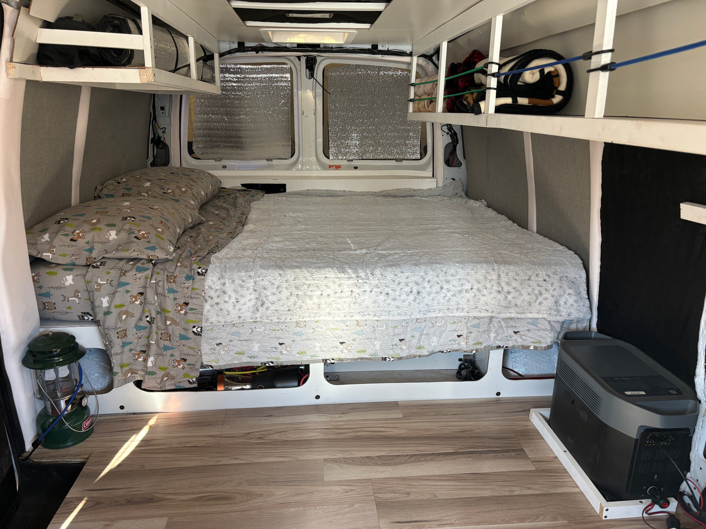 This RV rental interior shows a comfy bed, overhead storage, and an EcoFlow power station for vanlife adventures.