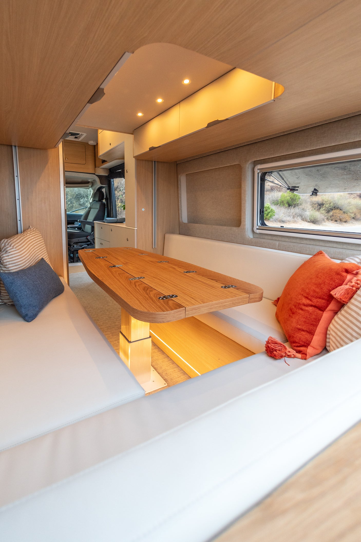 Experience an RV rental! Modern camper van interior with a bright dinette, comfy benches, and natural light from exterior views.