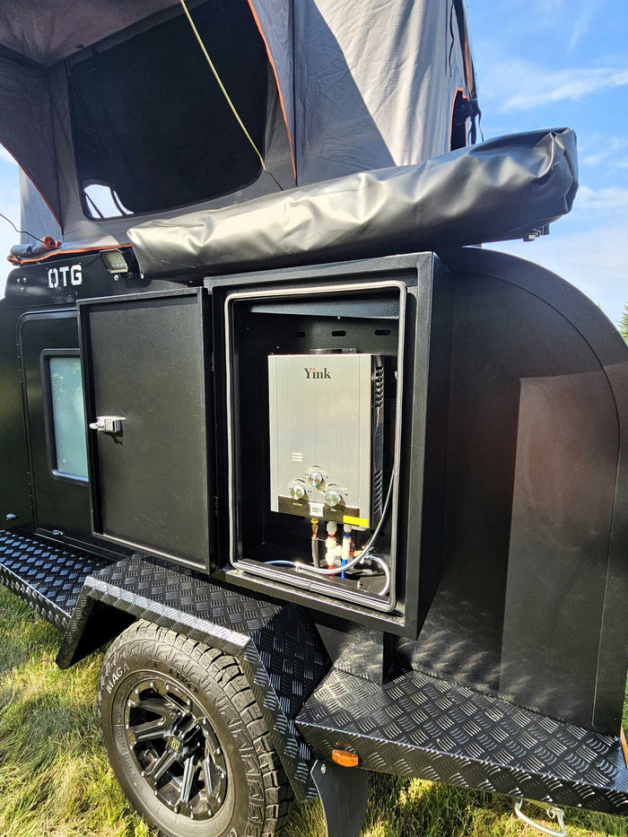 ready for adventure.|Black OTG teardrop RV rental featuring an external Yink water heater and rooftop tent. Ready for adventure.|View inside an RV rental's rear hatch revealing a black outdoor kitchen: pull-out stove