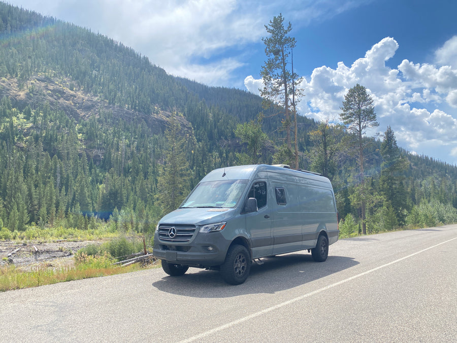 Adventure-ready Mercedes Sprinter rv rental parked on a scenic mountain road with dense forest views and a faint rainbow.|Stylish grey custom camper van
